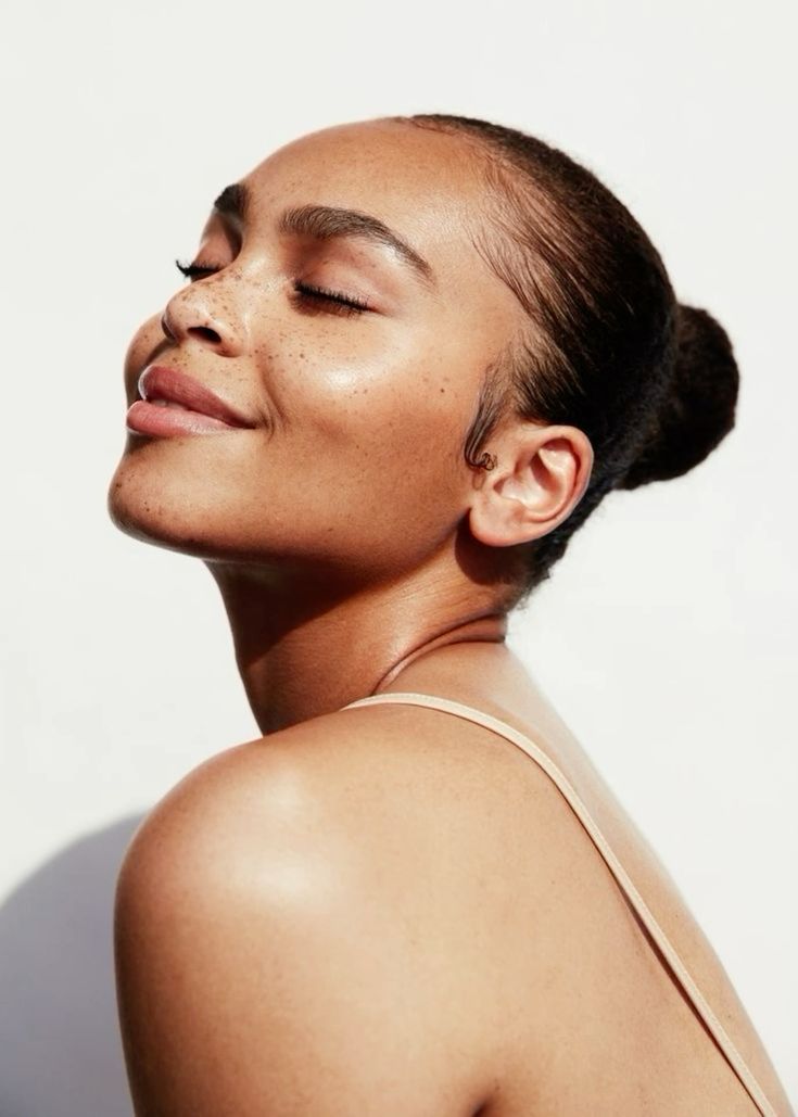 Woman with freckled, radiant skin tilting her head towards the light