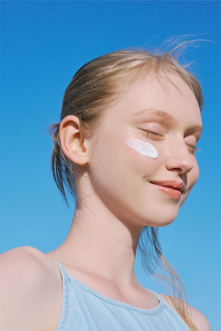 Smiling woman with a swipe of moisturiser on her cheek against a clear sky